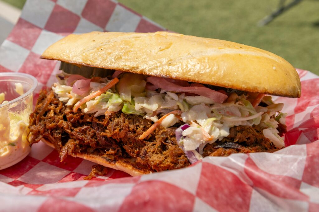pexels-photo-34495401-34495401 Tasty pulled pork sandwich topped with coleslaw on checkered paper outdoors.